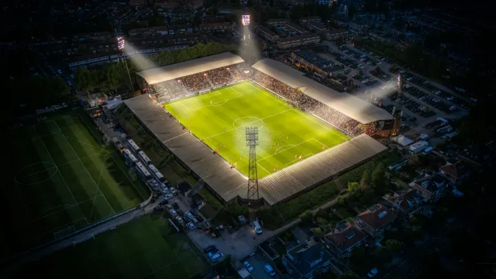 An aerial view of a brightly lit soccer stadium at night in a residential area