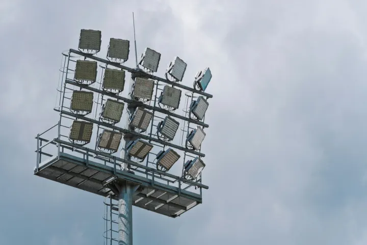 A tall stadium floodlight tower against a cloudy sky