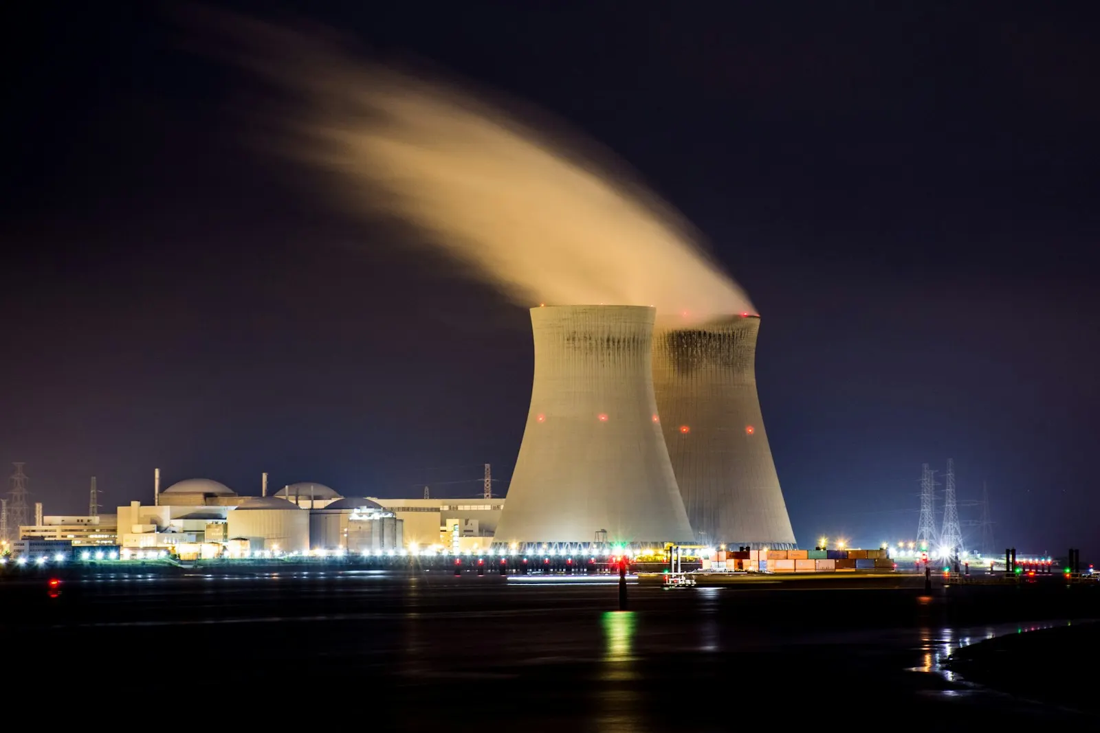 Two nuclear cooling towers emitting steam at night beside a dark river